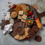 The full s'mores charcuterie board, piled high with graham crackers, chocolate, marshmallows, cookies, candies, and spreads.