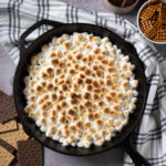 A cast iron skillet of s'mores dip with graham crackers and pretzels.
